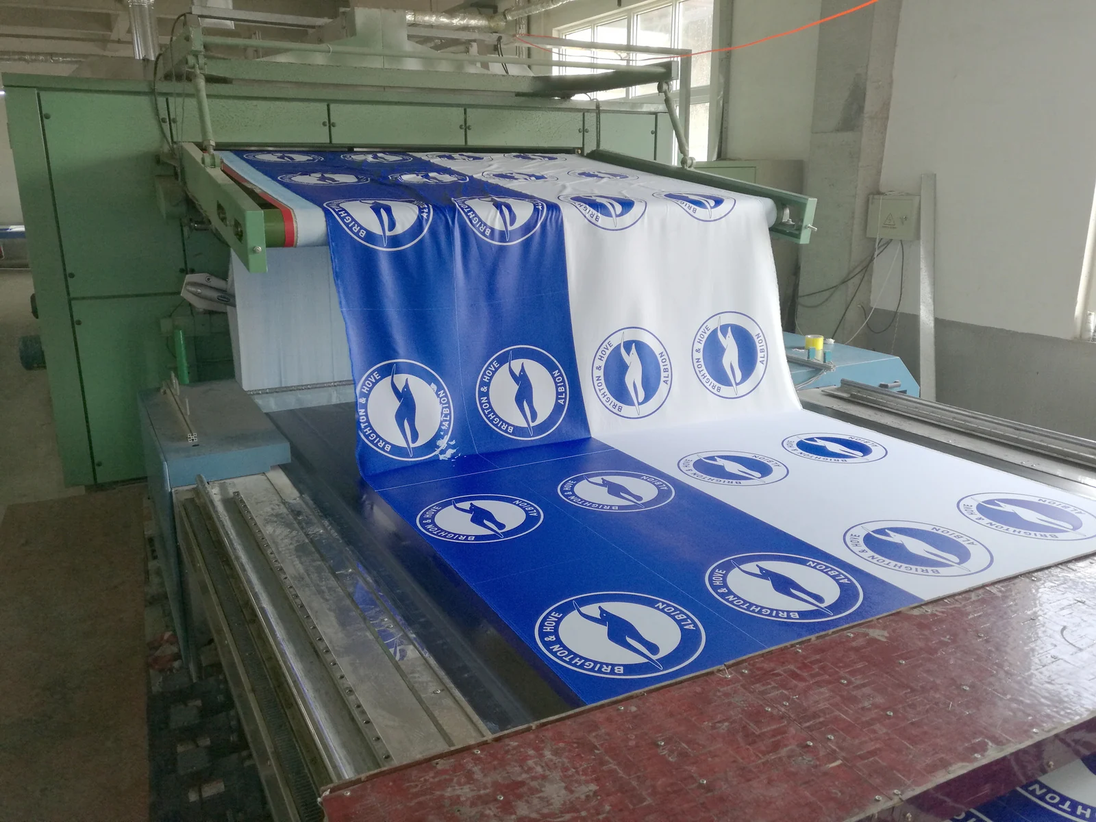 Industrial flag production machine handling blue and white Brighton and Hove Albion flag fabric.
